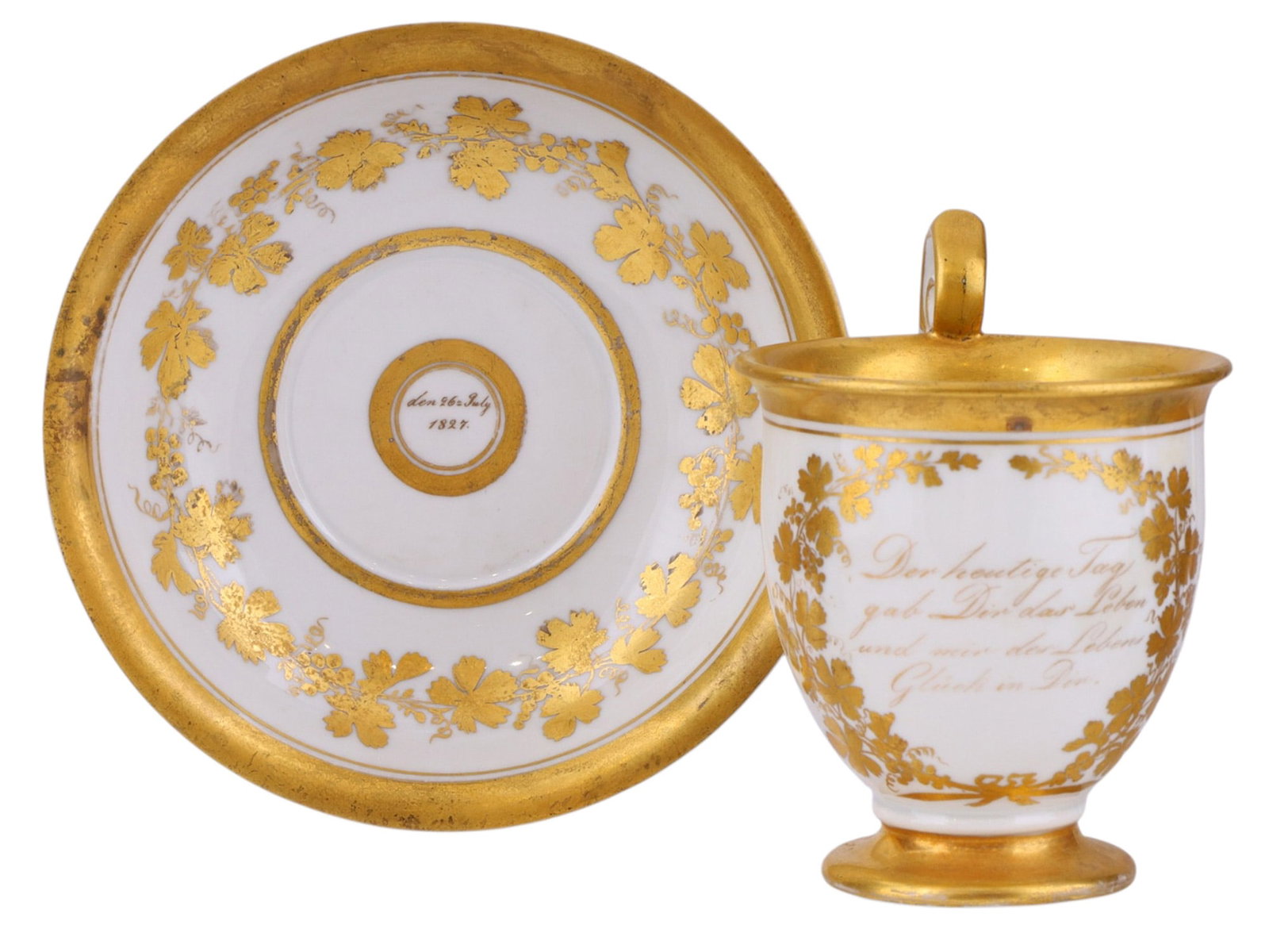 A GERMAN PORCELAIN GILT PRESENTATION CUP AND SAUCER, DATED 1827: The cup of slightly flared form with loop handle, richly gilt to the interior and rim, the exterior decorated with gilt vine and foliate garlands enclosing a German inscription, the saucer en suite wi
