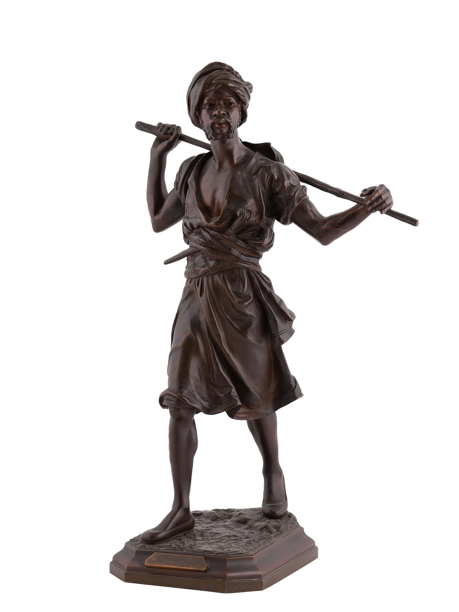 AN EMILE PINEDO FRENCH ORIENTALIST BRONZE SCULPTURE "ARABE EN MARCHE", LATE 19TH CENTURY: Depicting a standing Arab figure in motion, modeled wearing a turban and flowing robes while carrying a long staff across his shoulders. The figure is rendered with pronounced naturalism and animated 