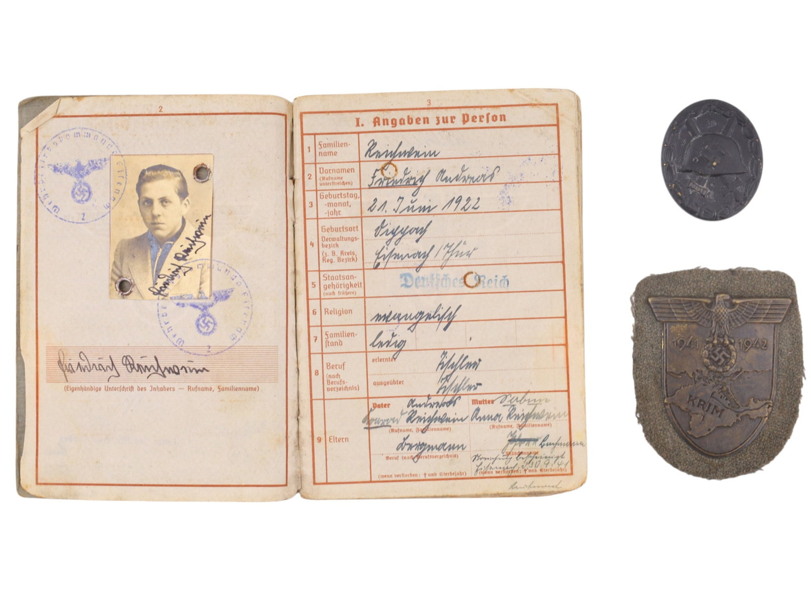 A GERMAN WEHRPASS GROUPING WITH WOUND BADGE AND CRIMEA CAMPAIGN SHIELD: A wartime German Wehrmacht grouping comprising a Wehrpass (military service record book) issued to Friedrich Reischwein (born 21 June 1922), together with a Black Wound Badge (Verwundetenabzeichen in 