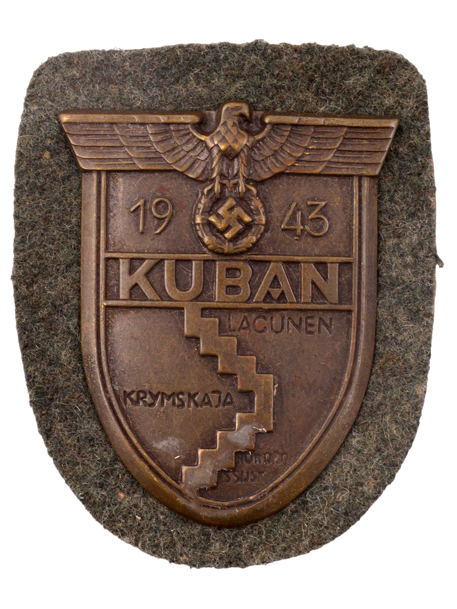 A GERMAN WWII KUBAN CAMPAIGN SHIELD, 1943: A German WWII Kuban Campaign Shield, 1943, mounted on field-gray wool backing with paper-covered reverse. The stamped bronze-toned shield is surmounted by the German eagle and swastika above the dates