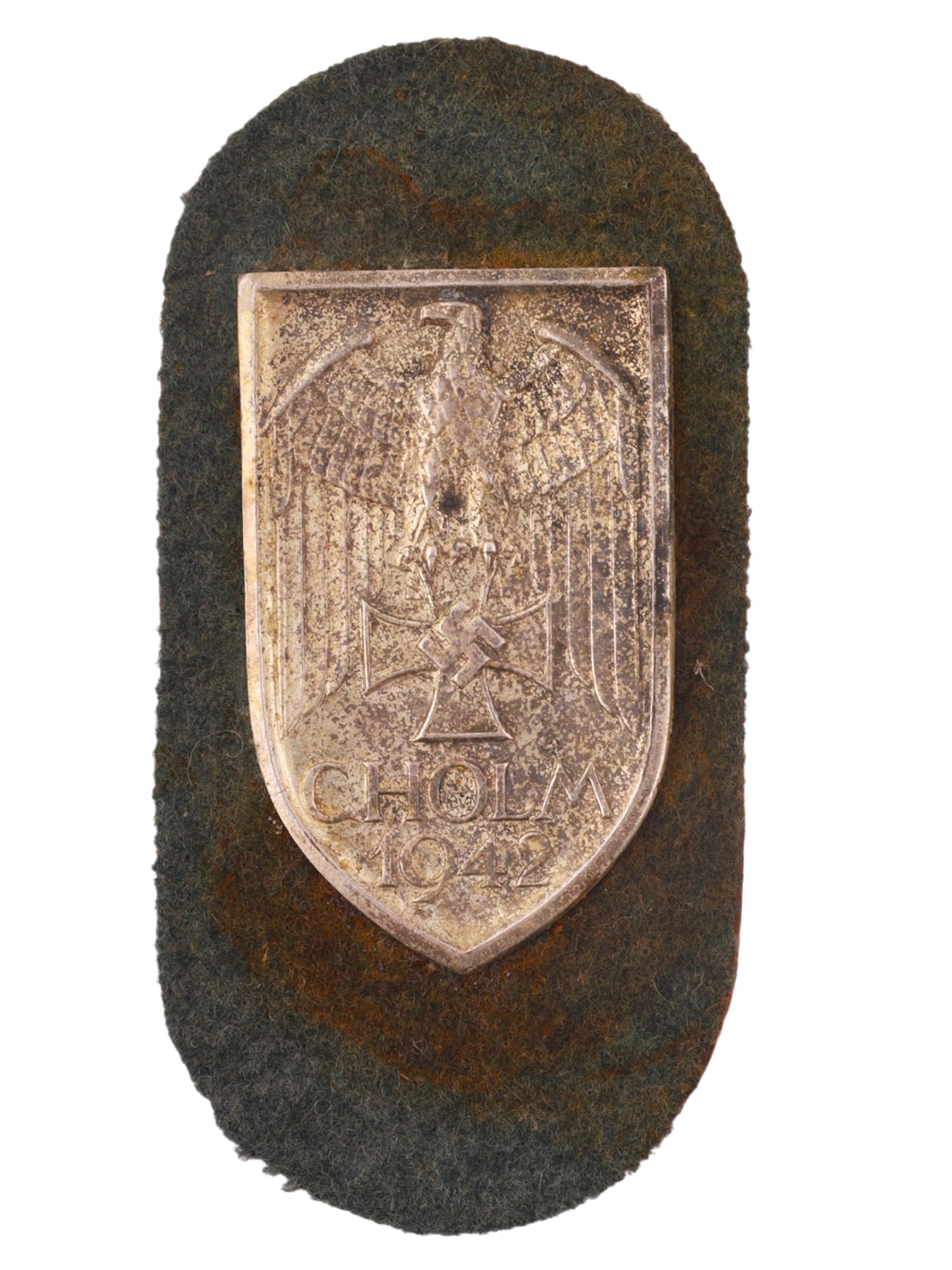 A GERMAN CHOLM SHIELD (CHOLMSCHILD), 1942, THIRD REICH PERIOD: Constructed of die-struck silvered metal in the form of a shield mounted on its original field-grey wool backing. The obverse bears the inscription "CHOLM 1942" and depicts an Iron Cross superimposed 