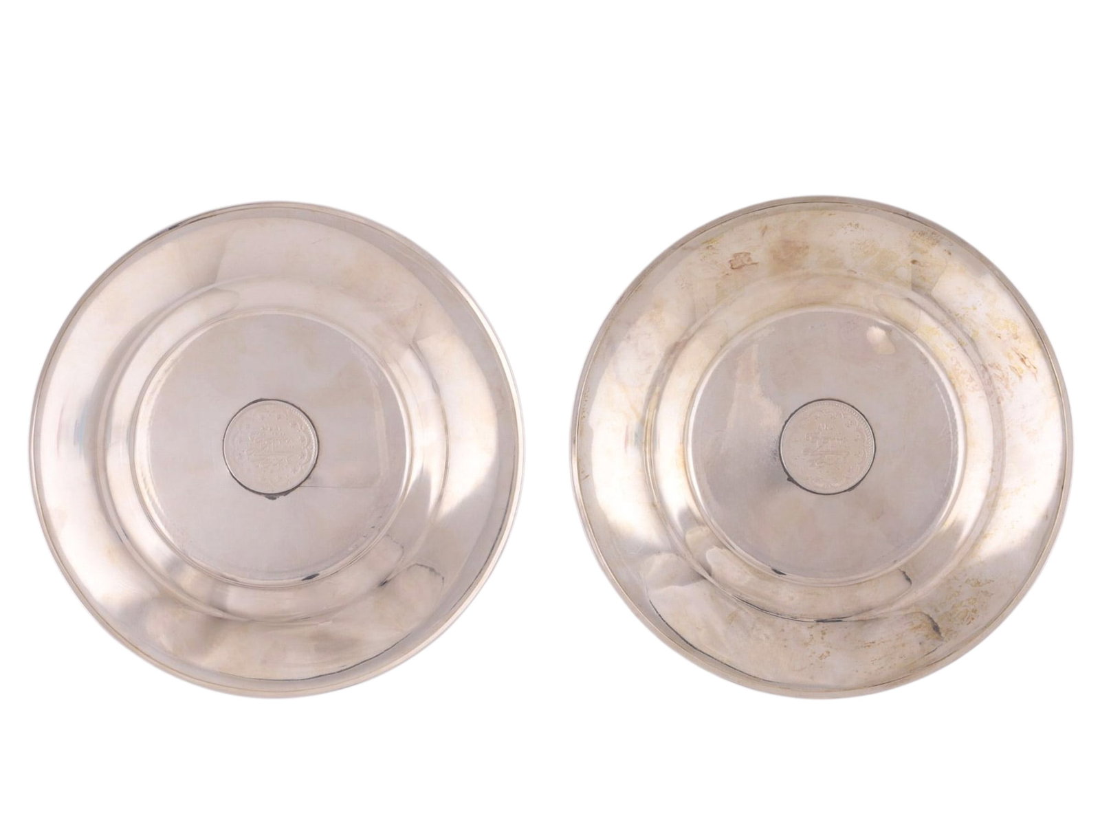 A PAIR OF TURKISH SILVER PLATES WITH COINS AND TUGHRA MARKS: A matched pair of Ottoman silver dishes of shallow circular form with gently rising sides, each centered with a mounted silver coin bearing a tughra and Arabic inscriptions. The coins are set within t