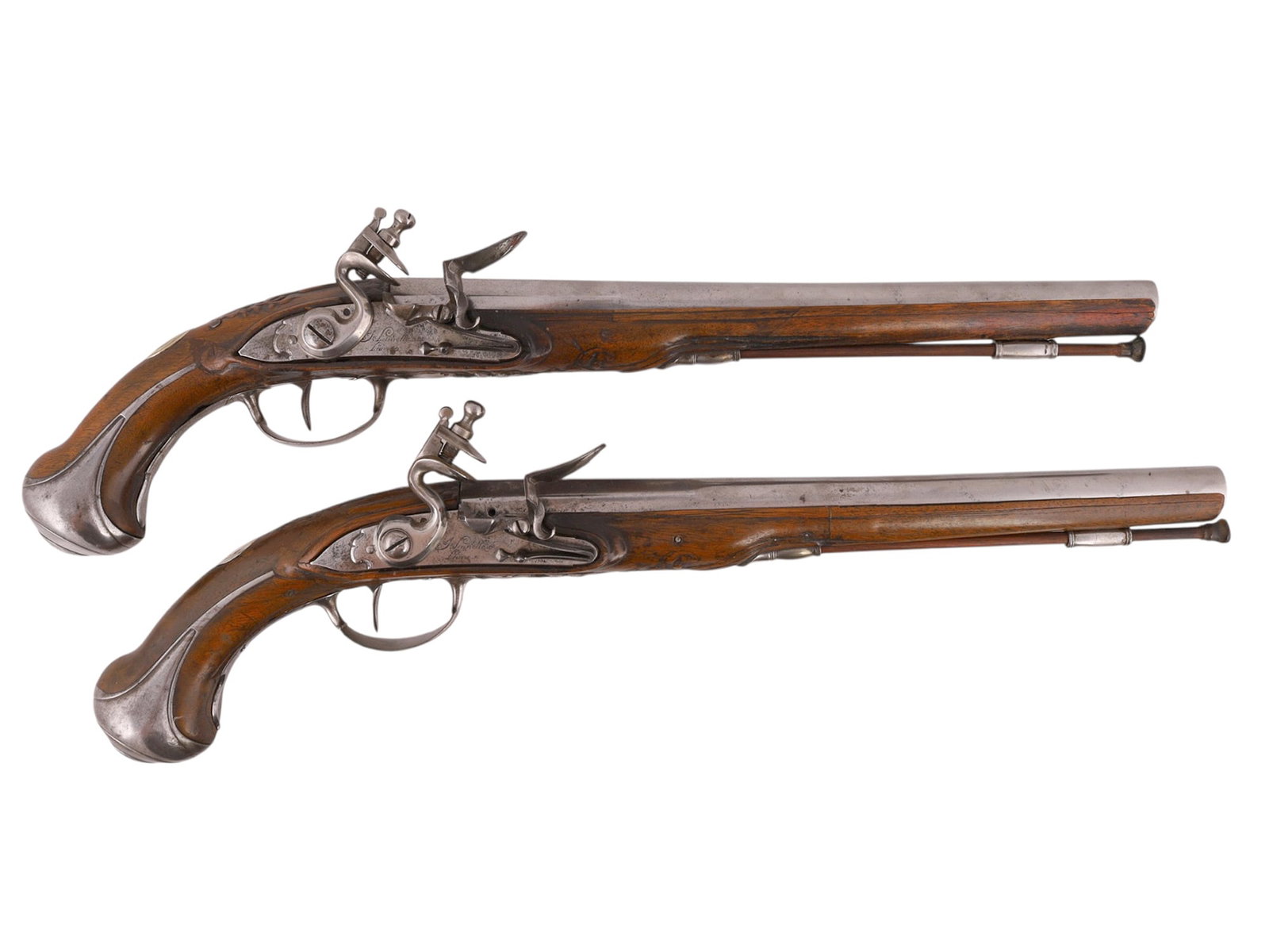 A PAIR OF MATCHING FLINTLOCK PISTOLS, FRENCH, MID-18TH CENTURY: With round smoothbore barrels retained by barrel pins to full carved walnut stocks, each fitted with finely engraved flintlock mechanisms signed by the gunsmith beneath the pan. The pistols feature ir