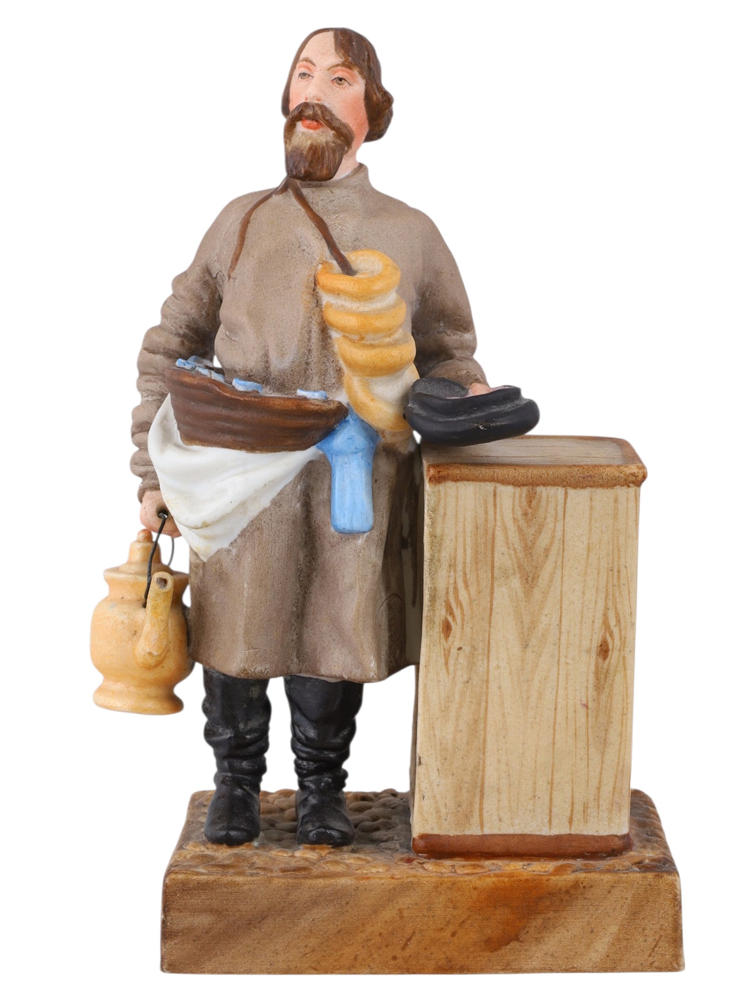 A RUSSIAN KUZNETSOV/GARDNER PORCELAIN FIGURE OF A SBITEN VENDOR, 19TH CENTURY: A russian figure produced by the Kuznetsov Porcelain factory shortly after their acquisition of of Gardner. The figure depicts a Sbitenshchik (sbiten vendor) leaning against a wooden stand, his cap tu