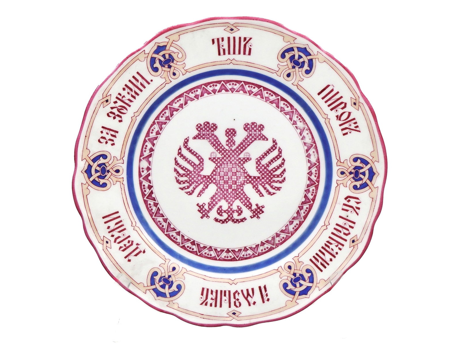 A RUSSIAN PORCELAIN PLATE WITH A PROVERB, KORNILOV BROS., 1861-1884: Kornilov Brothers Factory, St. Petersburg, Late 19th Century, 1890–1900.A circular porcelain plate with a scalloped edge, richly decorated in raspberry red, cobalt blue, and gilt. The central me