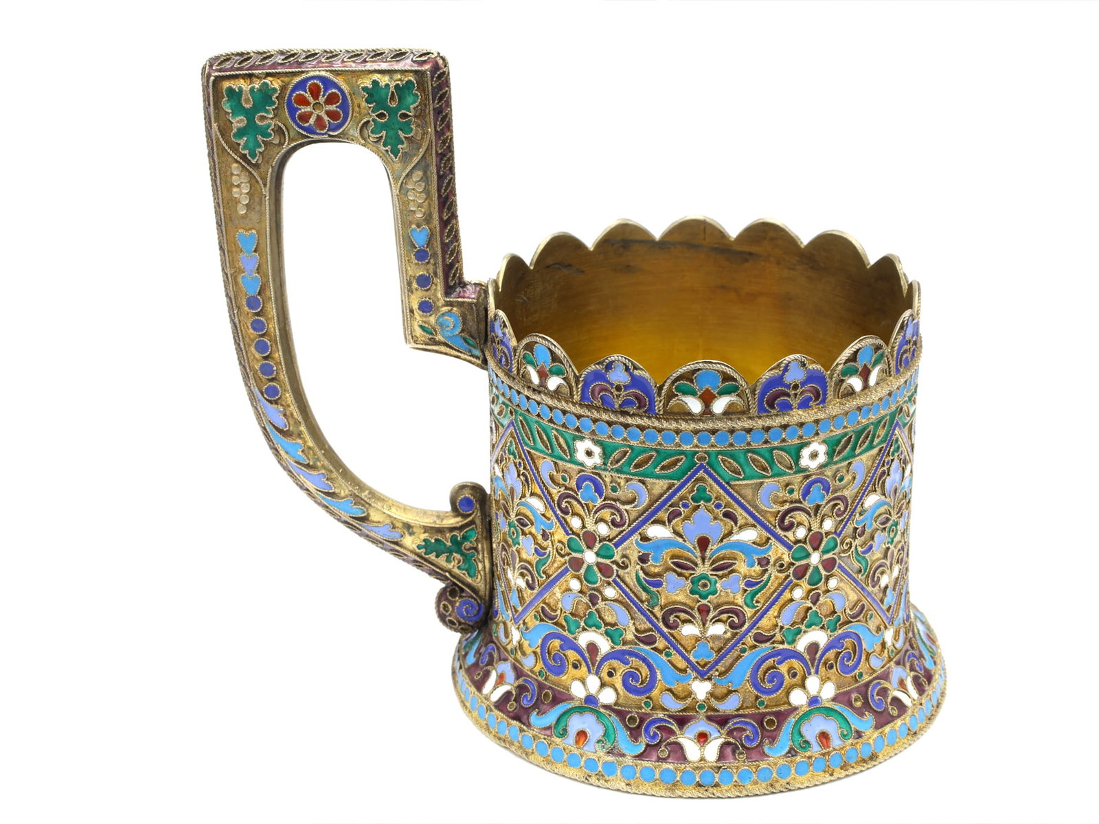 A RUSSIAN PARCEL-GILT-SILVER AND CLOISONNE ENAMEL TEA GLASS HOLDER: Russia, circa 1900. Of tapering cylindrical form with a flared base and tall angular scroll handle. The body is richly decorated with repeating diamond-shaped panels enclosing stylized flowerheads and
