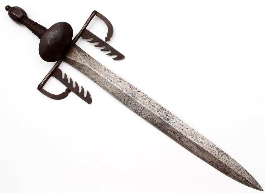 LARGE EUROPEAN LEFT HAND DAGGER WITH SWORD CATCHERS: Massive left hand dagger with its iron hilt mounts and two large sword catching devices protruding from the cross guard towards the blade. Broad double edged blade with central reinforcement ridge, bo