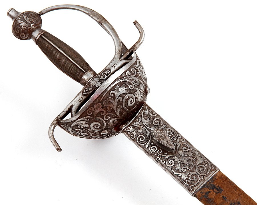 FINE CHISELED SPANISH TOLEDO CUPHILT RAPIER SWORD: With very fine hand chiseled steel hilt and scabbard mounts having elaborate floral motifs. Strong broad double edged blade engraved and dated on one side. Original leather scabbard showing light wear