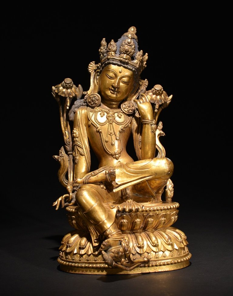 A GILT-BRONZE FIGURE OF GUANYIN: The bronze figure is seated on a double lotus base. Wearing traditional robes and designs, holding a small artifact in its left hand. There is a double vajra on the base. 10 1/4 in. (26.1 cm) tall. Mi