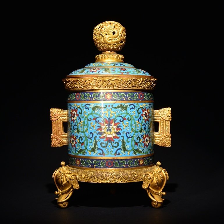 A GILT-BRONZE CLOISONNE ENAMEL INCENSE BURNER: The burner is cylinder-shaped and the exterior is decorated with numerous imperial designs. The cover of the burner is decorated with a dragon in a shape of a sphere. 13 3/8 in. (34 cm) tall. Qing Dyn