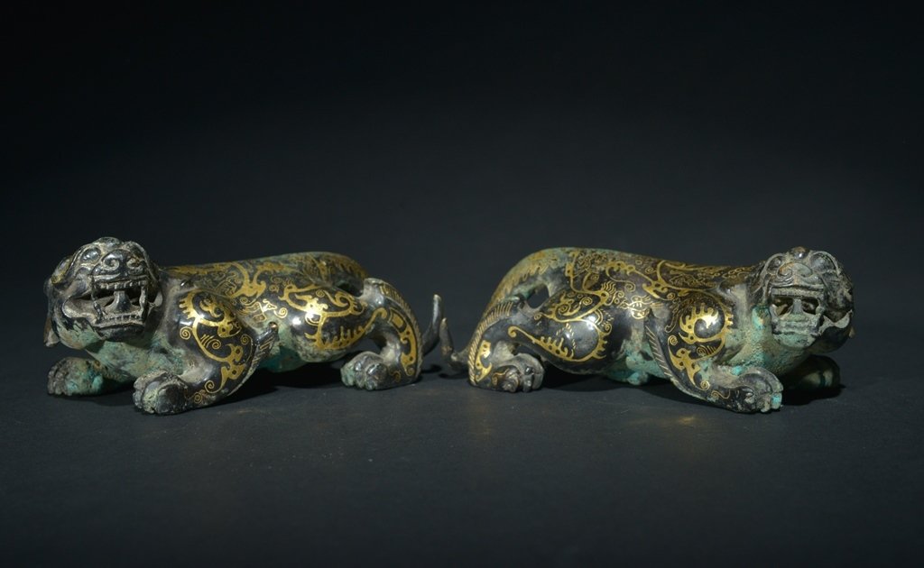 A PAIR OF GOLD-INLAID -BRONZE MYTHICAL BEASTS: The carving are two mythical beasts sitting. The exterior is decorated with imperial designs. 2 1/16 in. (5.2 cm) tall, 4 15/16 in. (12.5 cm) long. 2 in. (5.1 cm) tall, 5 in. (12.7 cm) long. Han Dynas