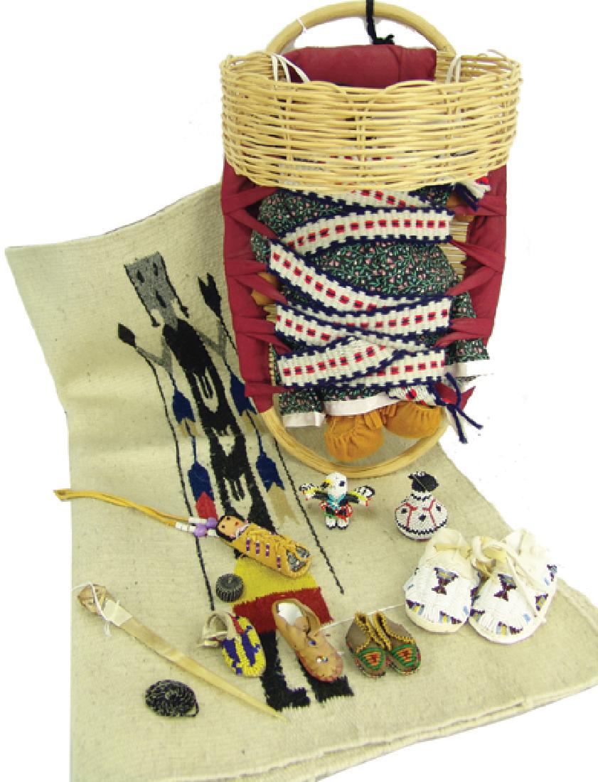 Box Lot of Miscellaneous Indian Items: Various Ages, Includes a Navajo cradle board and doll by Delores Honga, a 1970s "Trader's Yei" rug, several small beaded items, and an 8" bone awl. Good condition. Largest 58" x 28"