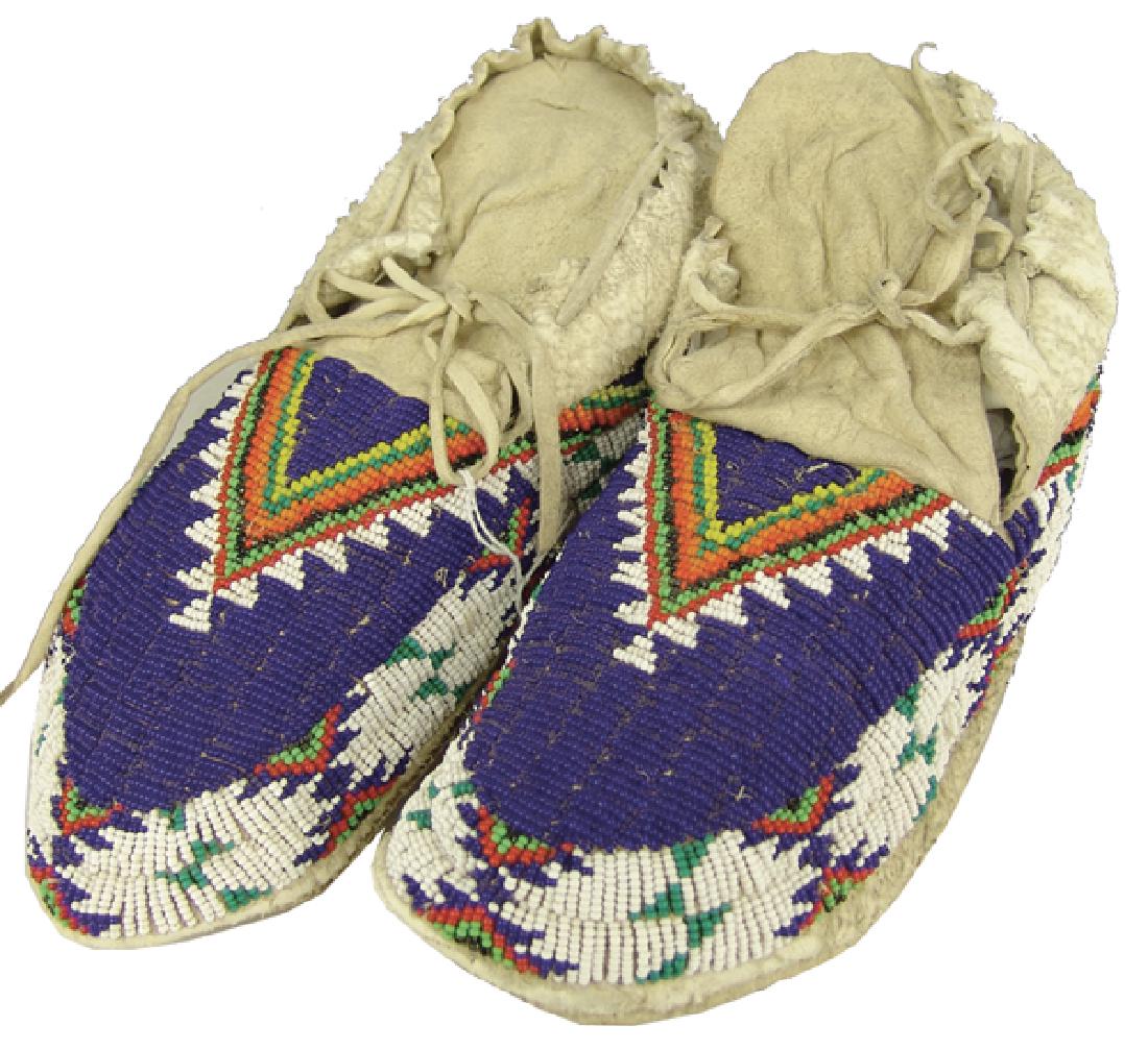 Plains Beaded Moccasins: Traditional pair of sinew sewn and lazy stitch beaded hard soled moccasins with classic geometric designs on the the vamps and around the soles. Very good condition, with very minor bead loss/damage.C