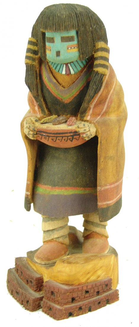 Hopi Kachina Carving: Hand carved and painted, "one-piece" style cottonwood root "Hano-Mana" doll shown holding a basket of corn. The base is carved to represent a Pueblo. Good condition.Ca. 199210-1/2"