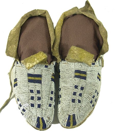 Arapaho Beaded Moccasins: Pair of rare sinew sewn and lazy stitch beaded white ground moccasins with hard rawhide soles and traditional geometric designs; good condition, minor bead loss. 9" Circa Early 1900s