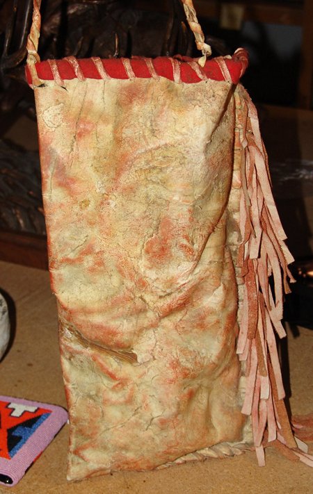 Plateau Parfleche Bag: Mid 1900s, Rare formed buffalo rawhide cylindrical container with fringed edge and tradecloth trim. Good condition, one side of strap disattached. 15" x 9" + handle