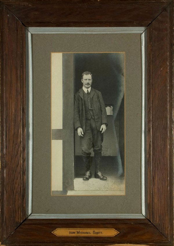 A period b&w photograph of the Hon. Michael Scott,: A period b&w photograph of the Hon. Michael Scott, mounted in the original frame with a gilt plaque titled HON: MICHAEL SCOTT, the image 37 by 19cm., 14 1/2 by 7 1/2in.