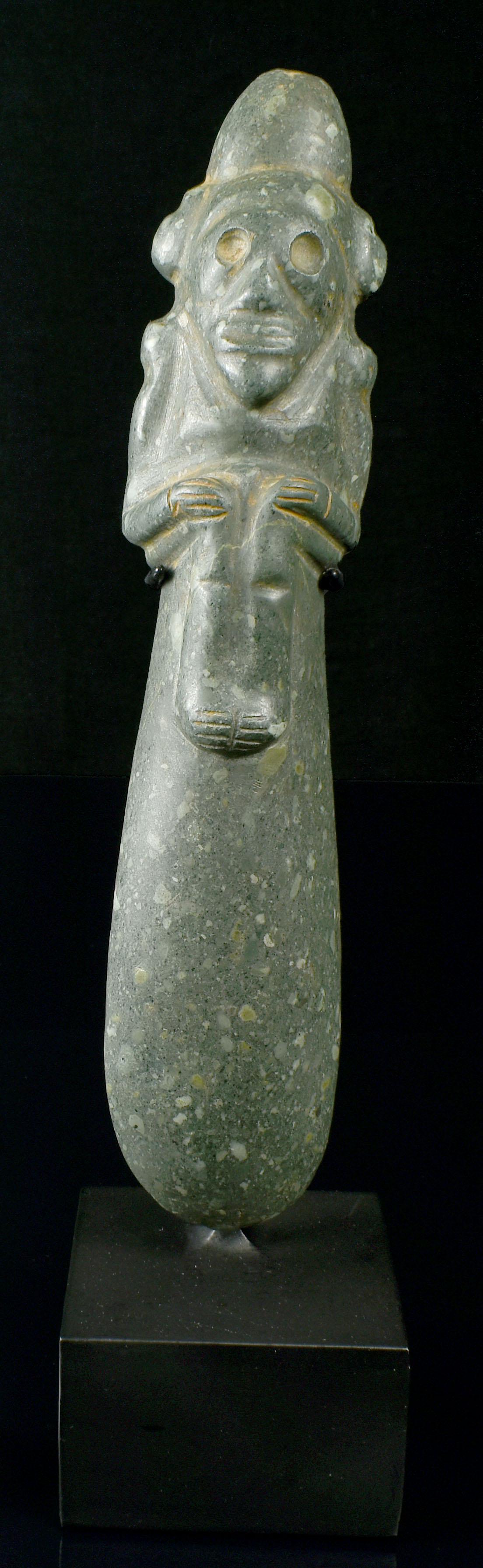 Pre Columbian Taino Stone Scepter with Zemi God: A magnificent Pre Columbian Taino Green Porphyry Stone Scepter carved as a stylized Zemi God figure. The Zemi, with deeply carved features, sits in a crouching position with his arms folded into