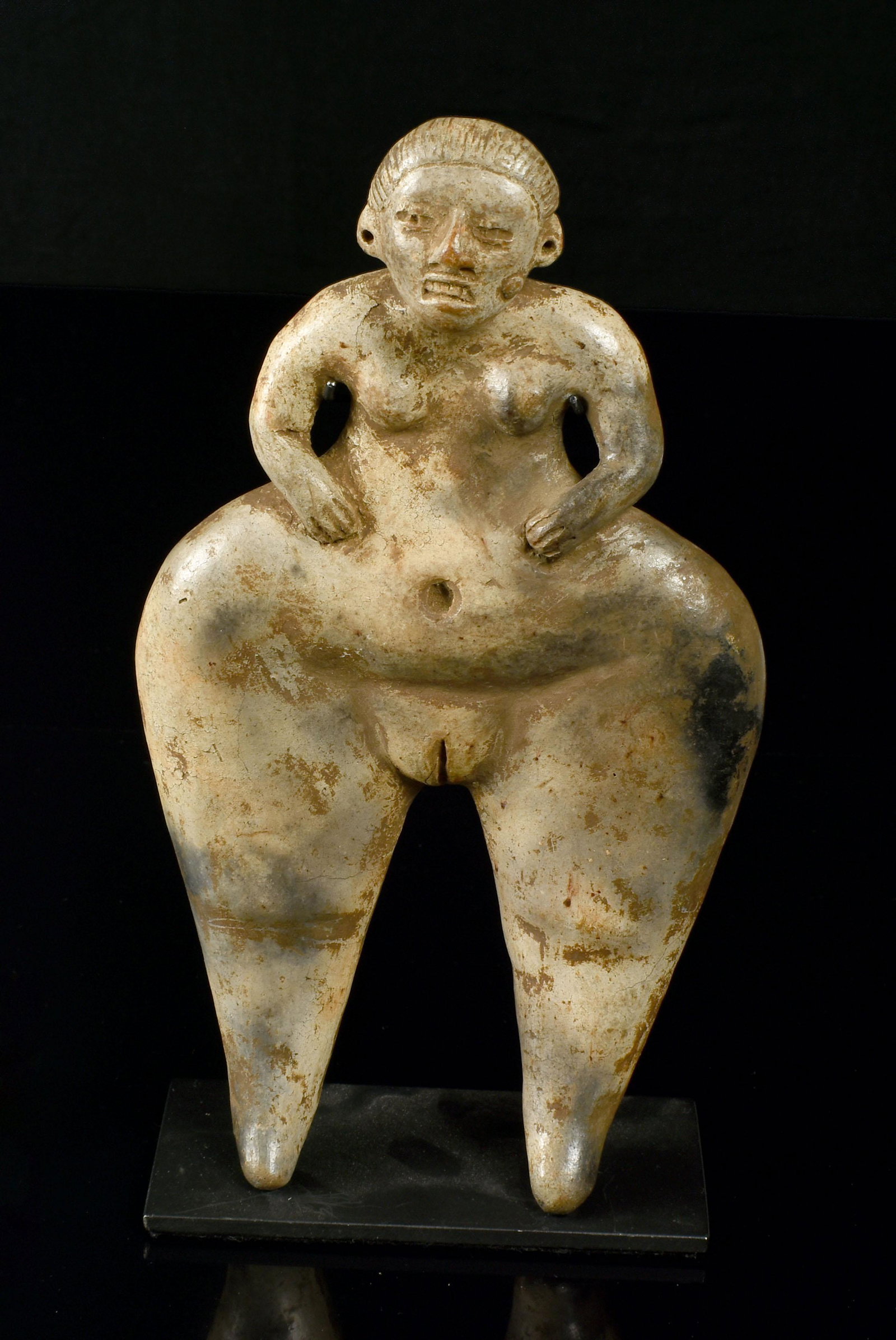 Style of Pre Columbian PreClassic Venus Mother Goddess: Pre Columbian Style PreClassic Pottery Figure. A Labret adorns one cheek and both ears are perforated. The open mouth shows a row of grimacing teeth. The disproportioned 