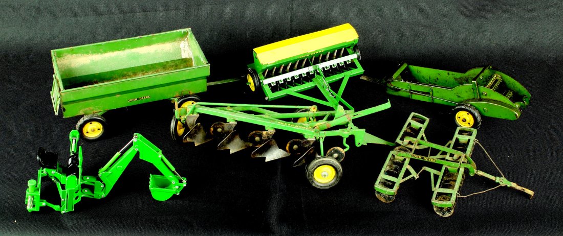 Assortment of Vintage John Deere Toy Farm implements: Includes a Backhoe attachment, planter, 4-blade plow, roller disc plow, spreader, and a wagon. All from the Nick Hadden Collection of Vintage Toys & Models. 