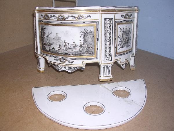 HOCHST DAMM BOUGH POT: An early 19th century Hochst Damm bough pot and pierced cover, painted in grisaille and sepia with an estuary scene central to the bow front and with flanking trophies, gold crowned wheel mark, 23cm w
