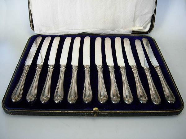 A CASED SET OF 12 CHEESE KNIVES, MAPPIN + WEBB: A set of twelve silver handled cheese knives by Mappin & Webb, Sheffield 1915, the handles of a stylized thread pattern, cased