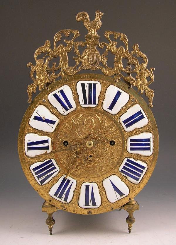 A FRENCH BRASS LANTERN TYPE CLOCK: A French brass lantern type clock, the gilt decorated dial with applied enamel numerals and pierced classical cresting, with associated later twin bell striking movement, raised on 4 turned feet, 35cm