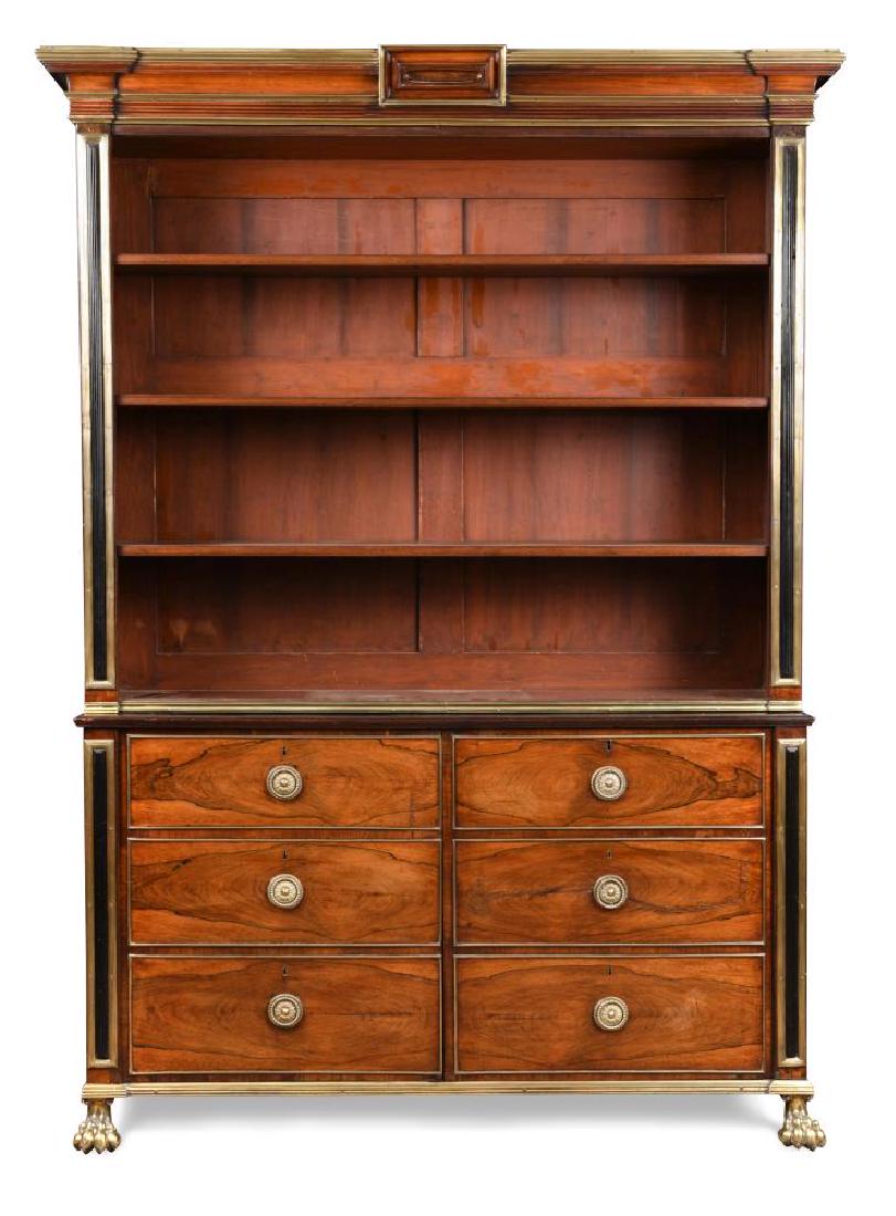A Regency rosewood bookcase in the manner of John: A Regency rosewood bookcase in the manner of John McLean, with brass mounted cornice, ebony stepped side panels outlined in brass to the boarded shelved back, above cupboards with faux drawer fronts,