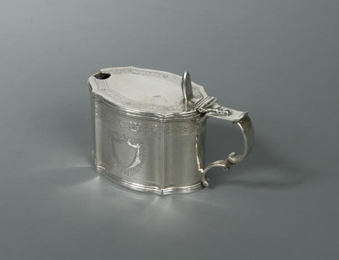 A Victorian silver mustard,: A Victorian silver mustard, by Charles Stuart Harris, London 1898, nominally oval in form with panelled sides decorated with two shield shaped cartouches, one monogrammed, bordered with bright cut dec