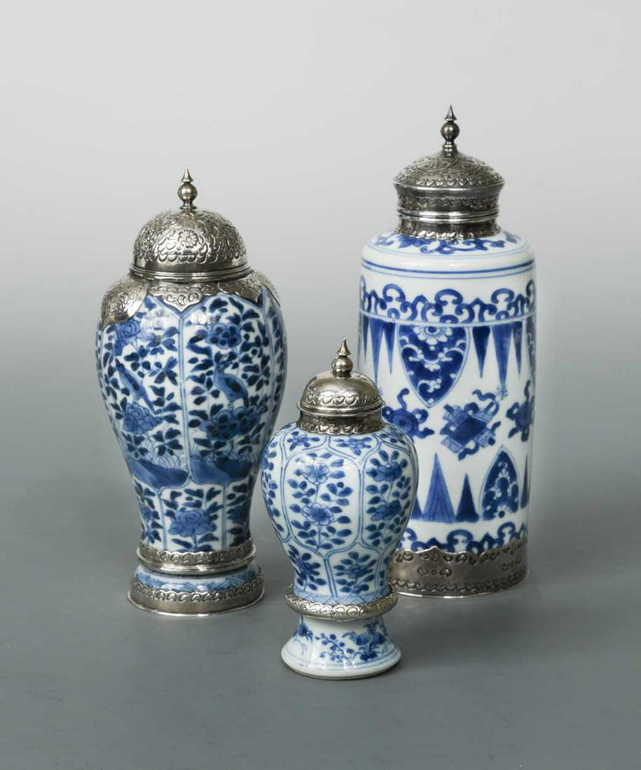 A Chinese blue and white export porcelain vase, Kangxi: cylindrical, painted with repeated Buddhist precious objects within leaf tips, the reduced neck with later metal mounts and cover, 20.5cm high; together with two other similarly mounted Kangxi baluste