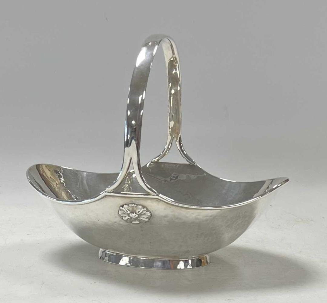 A George V silver â€˜Arts & Craftsâ€™ style silver bon bon dish, mark of A.E. Jones,: Birmingham 1914, of oval form with hammered finish and turned rim, simple fixed handle with rosettes by the split terminals, raised on a spread foot, 21 x 14cm excluding the handle, underside numbered