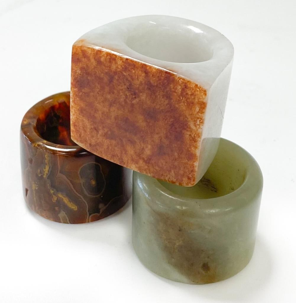 Three Chinese archer's rings,: Three Chinese archer's rings, comprising a mutton fat jade plain example 3.2cm diameter; a jasper example 3cm diameter; and a white mottled stone signet ring shape example with a brown mottled table 3