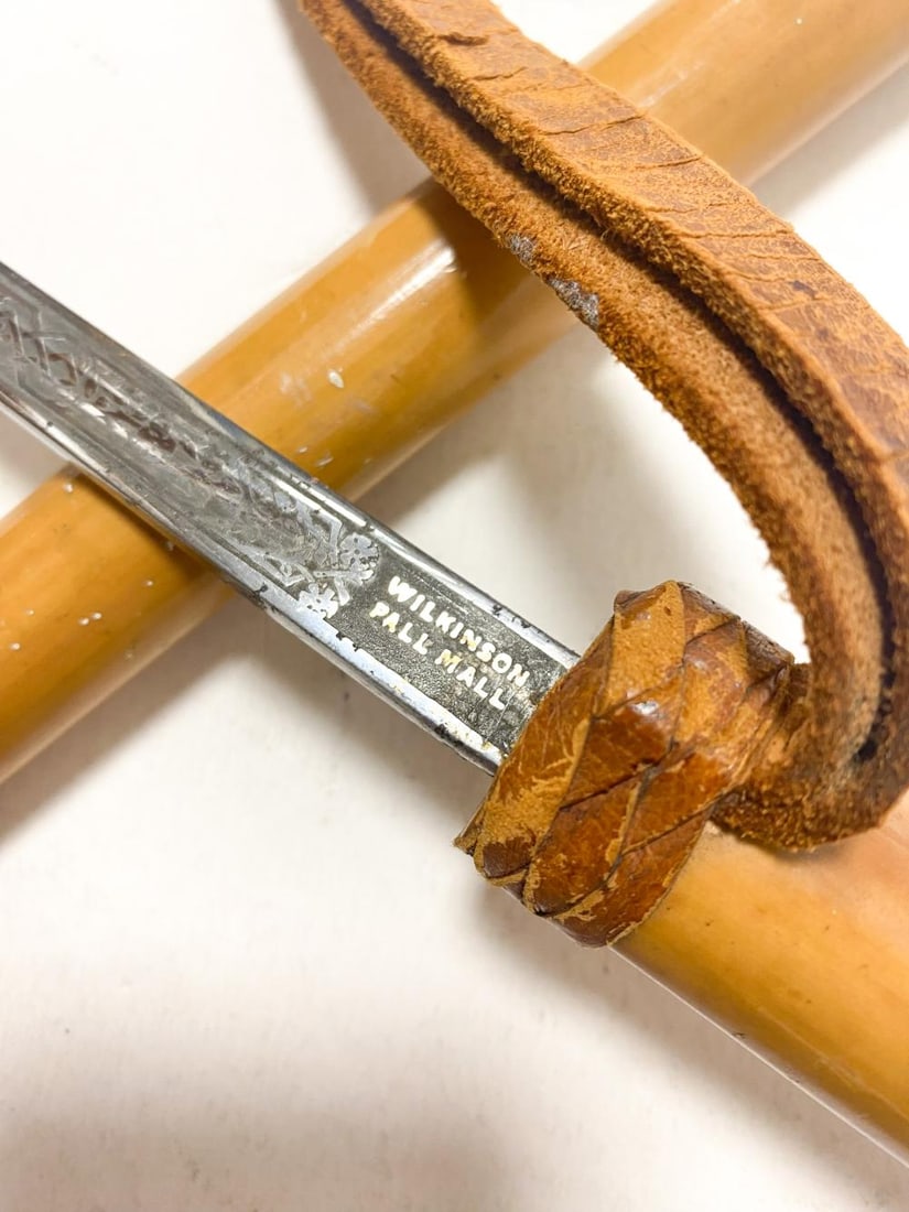 A sword stick or baton by James Smith & Sons, New Oxford Street, early 20th century,: A sword stick or baton by James Smith & Sons, New Oxford Street, early 20th century, the bamboo handle and scabbard concealing a tapering fullered Wilkinson blade, a leather strap handle 66cm long ove