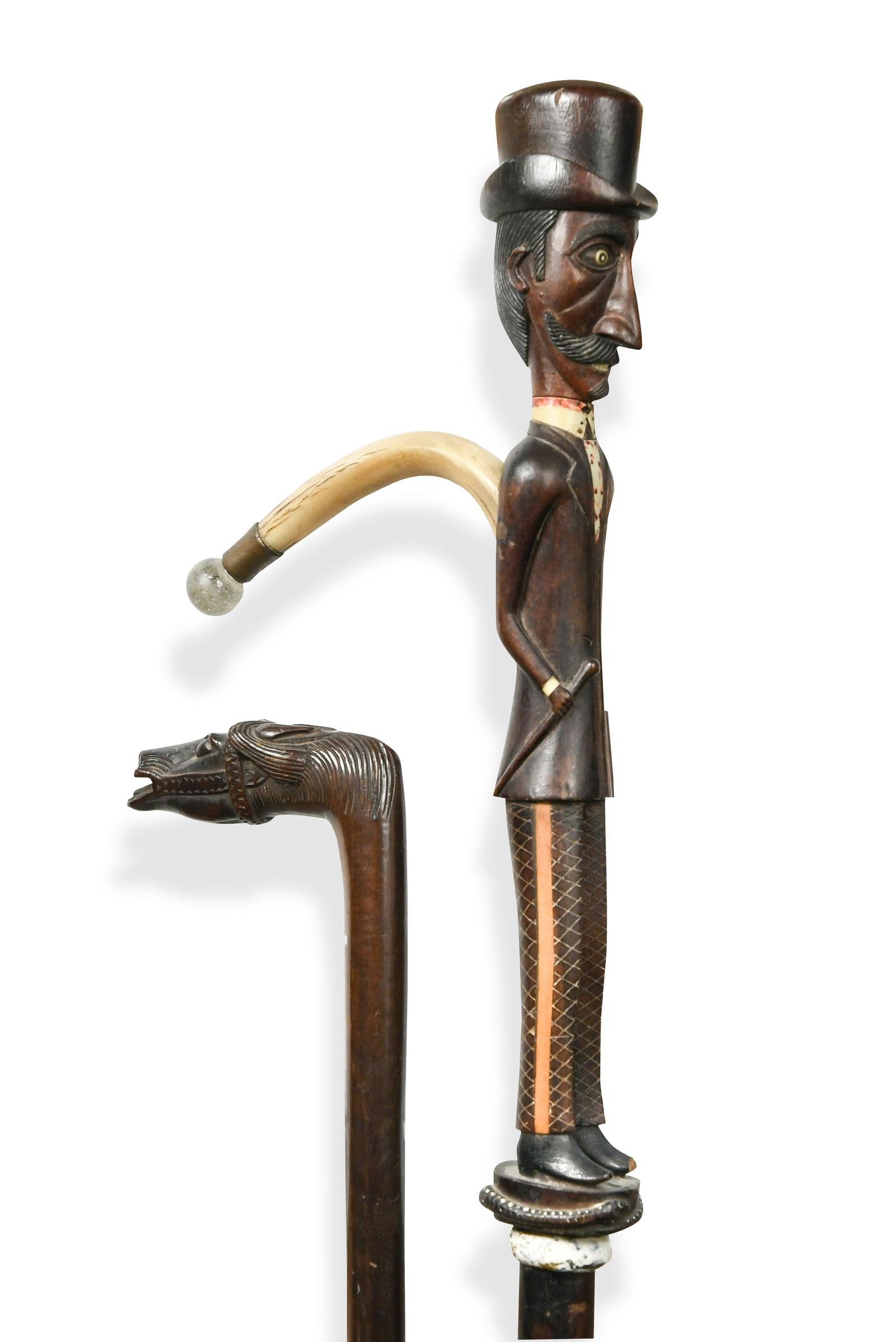 A Colonial hardwood walking stick with curving horn handle, early 20th century,: A Colonial hardwood walking stick with curving horn handle, early 20th century, the upper section carved as a full length gentleman in formal European dress holding a case and a stick, a top hat sitti