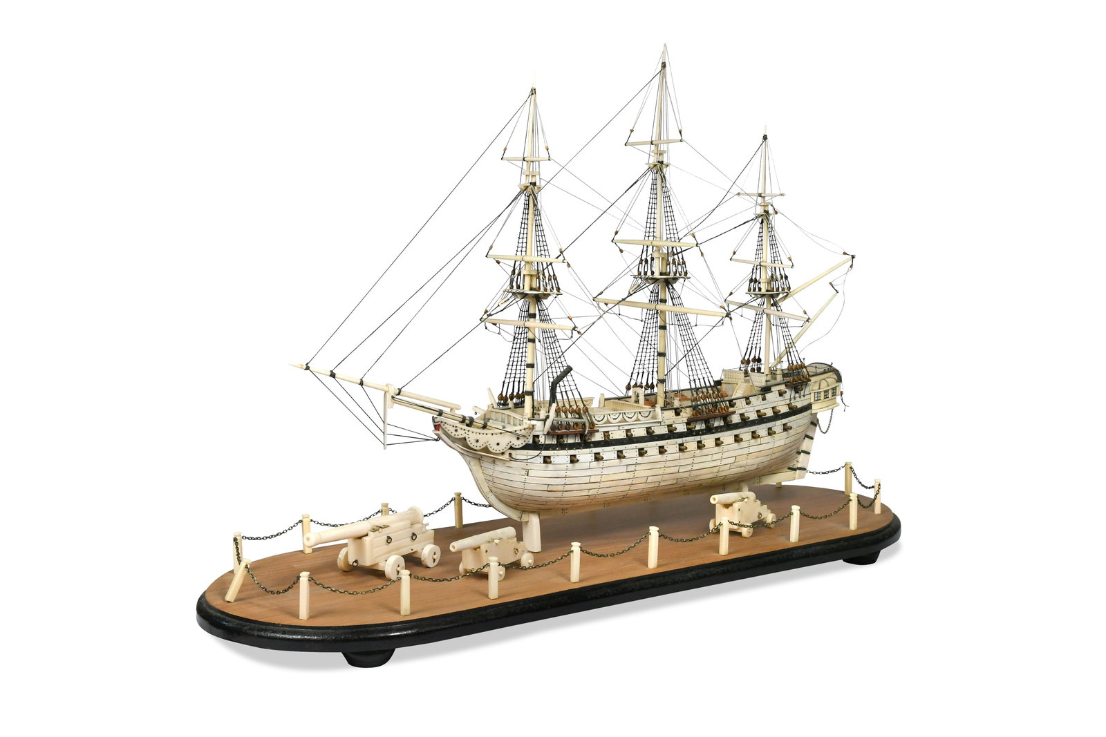 A Prisoner of War style bone model of a 68 guns ship, modern,: A Prisoner of War style bone model of a 68 guns ship, modern, with full rigging, mounted to a hardwood plinth base with chain link fence and three further carved bone cannon the ship 62cm long