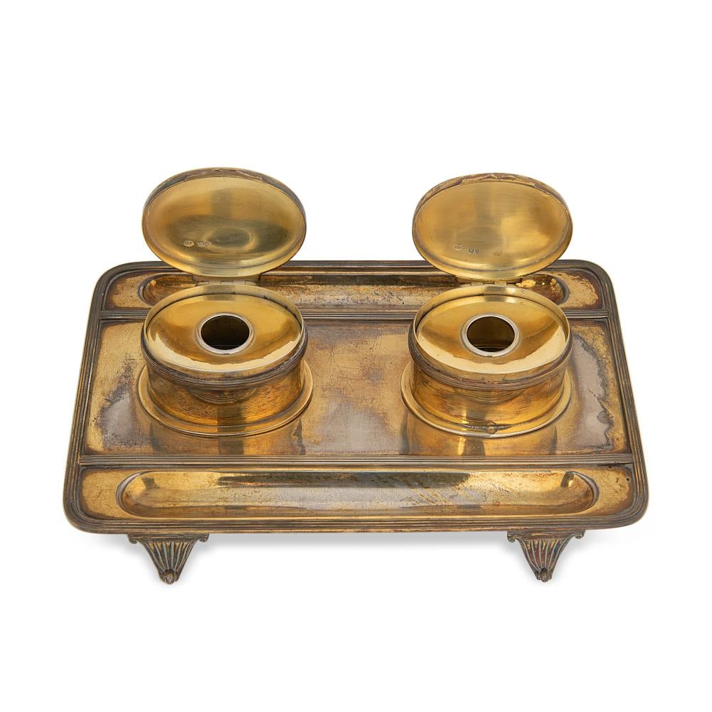 A Victorian silver gilt desk inkstand,: A Victorian silver gilt desk inkstand, mark of George Fox, London 1886, of rectangular form with turned corners and reeded border, two dished pen rests and two oval inkwells with glass containers and