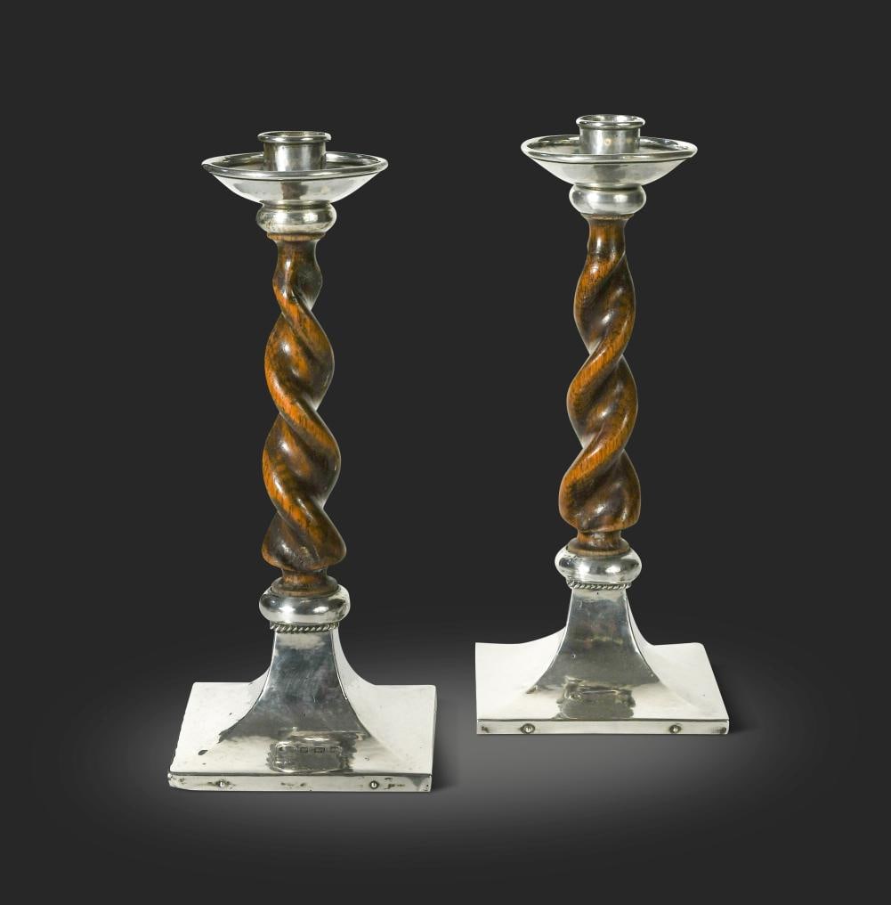 A pair of Arts & Crafts barley twist oak and silver mounted candlesticks, mark of A.E. Jones,: A pair of Arts & Crafts barley twist oak and silver mounted candlesticks, mark of A.E. Jones, each rising from planished square foot to twisted stem and circular planished drip-pan and sconce, each st
