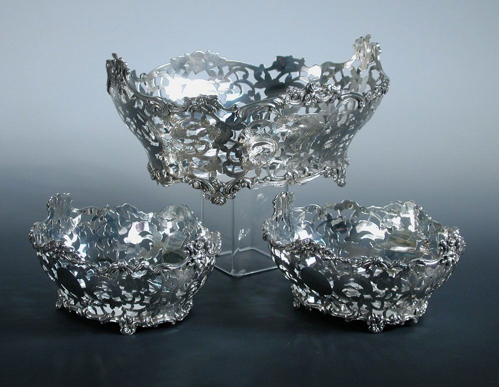 An Edwardian silver three piece garniture of baskets,: An Edwardian silver three piece garniture of baskets, by Charles Stuart Harris, London 1901/1902, comprising a large oval pierced basket of compressed oval shape below a floral scrolled edge, the cart