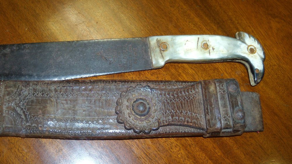A mid 20th century Collins 'Legitmus' machete and leath: A mid 20th century Collins 'Legitmus' machete and leather scabberd, the single edged blade stamped with the maker's name and No. 1293 below the horn handle with eagle head pommel, the leather scabberd