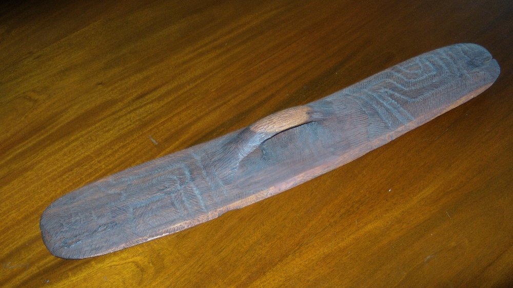An Aboriginal wooden shield,: An Aboriginal wooden shield, the handle hollowed out centrally to geometric patterns on one side of the elongated oval shape, the flat side with sinuous vertical chiselled lines, 78cm (30.75 in.) high
