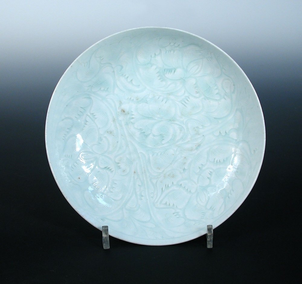 A Song dynasty ying ching dish: A Song dynasty ying ching dish incised on the cavetto and within the interior with scrolling flowers below a misty blue glaze, the glaze on the reverse dimpled, 19.5cm (7.75 in.) diameter