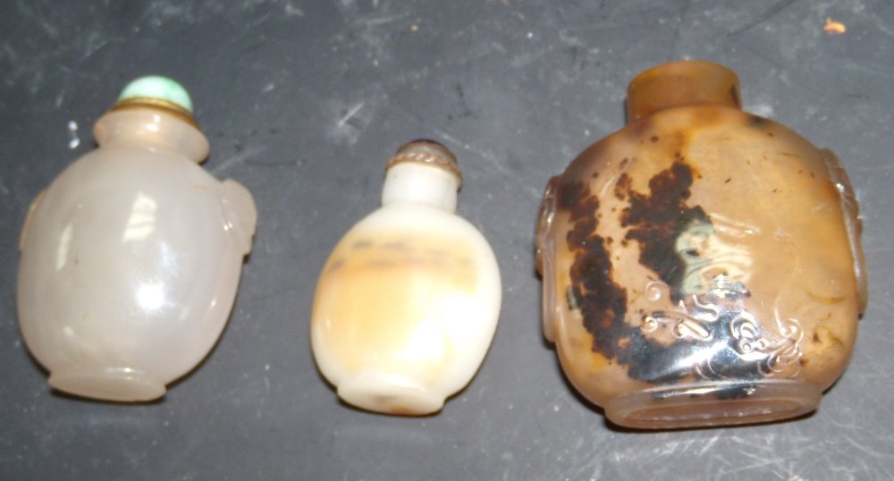 Two agate and a glass snuff bottle with two stoppers,: Two agate and a glass snuff bottle with two stoppers, one of grey stone with Buddhist lion mask handles, 6.5cm (2.5 in.) high, the other of toffee colour with dark brown inclusions carved with a drago