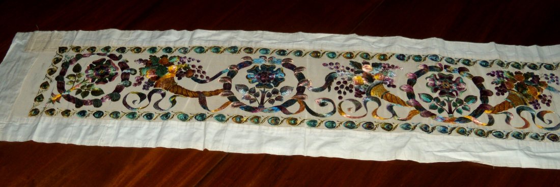 An Edwardian silkwork panel, dated 1909,: An Edwardian silkwork panel, dated 1909, worked with floral roundels alternating with cornucopia within peacock feather border banding on a white ground, a lable to one end inscribed 'Miss Edith Drumm