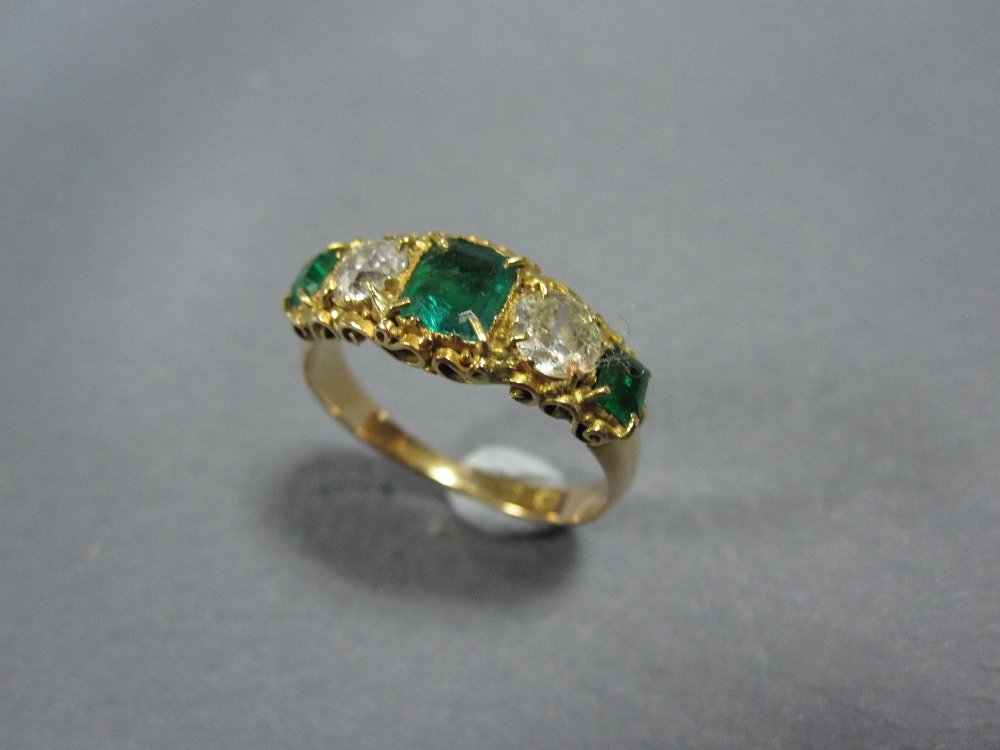 An emerald and diamond five stone ring,: An emerald and diamond five stone ring, the central emerald cut emerald in closed back setting flanked by old round brilliant cut diamonds and two smaller similarly set emeralds (one possibly a replac