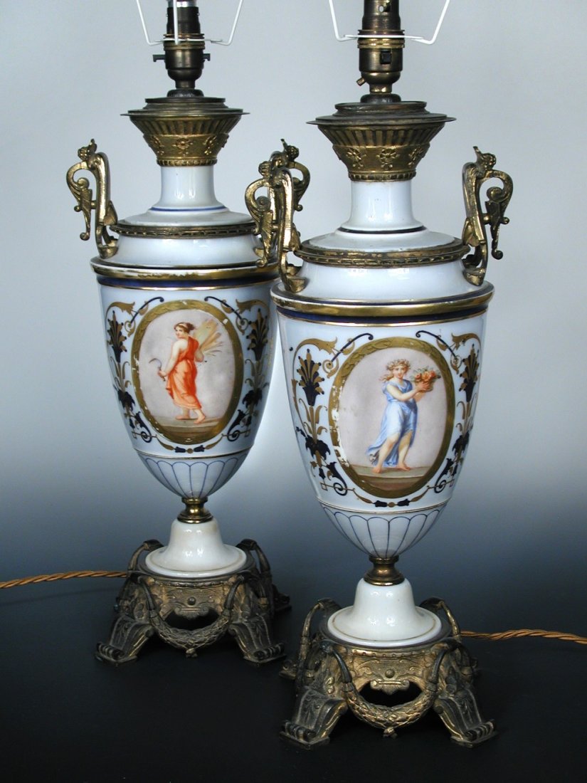 A pair of late 19th/early 20th century ormolu mounted: A pair of late 19th/early 20th century ormolu mounted Paris porcelain table lamps, each of the two handled baluster shapes with gilt and dark blue bands on a pale sky blue ground, one painted with an