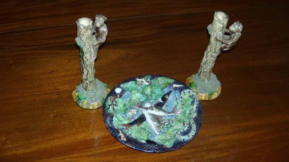 Mafra, Caldas, Portugal', a pair of candlesticks: Mafra, Caldas, Portugal', a pair of candlesticks together with a Palissy type dish, monkeys climbing up the tree trunks to peer into the nozzles, the circular bases in green and ochre, impressed marks