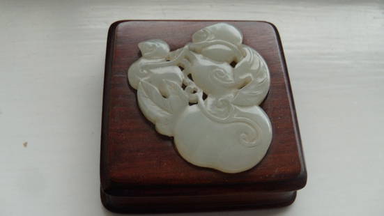 A hardwood mounted nephrite jade paperweight,: A hardwood mounted nephrite jade paperweight, the pale grey stone pierced and carved with a double gourd amongst its foliage and inset into a square cushion of red toned wood, 6 x 6cm (2.25 x 2.25 in)