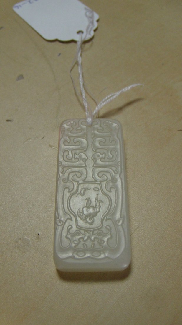 A white jade rectangular pendant,: A white jade rectangular pendant, carved in low relief with daodieh enclosing quatrefoil reserves, one side inscribed and the other with a bat flying over a pair of peaches, 5cm (2 in) high