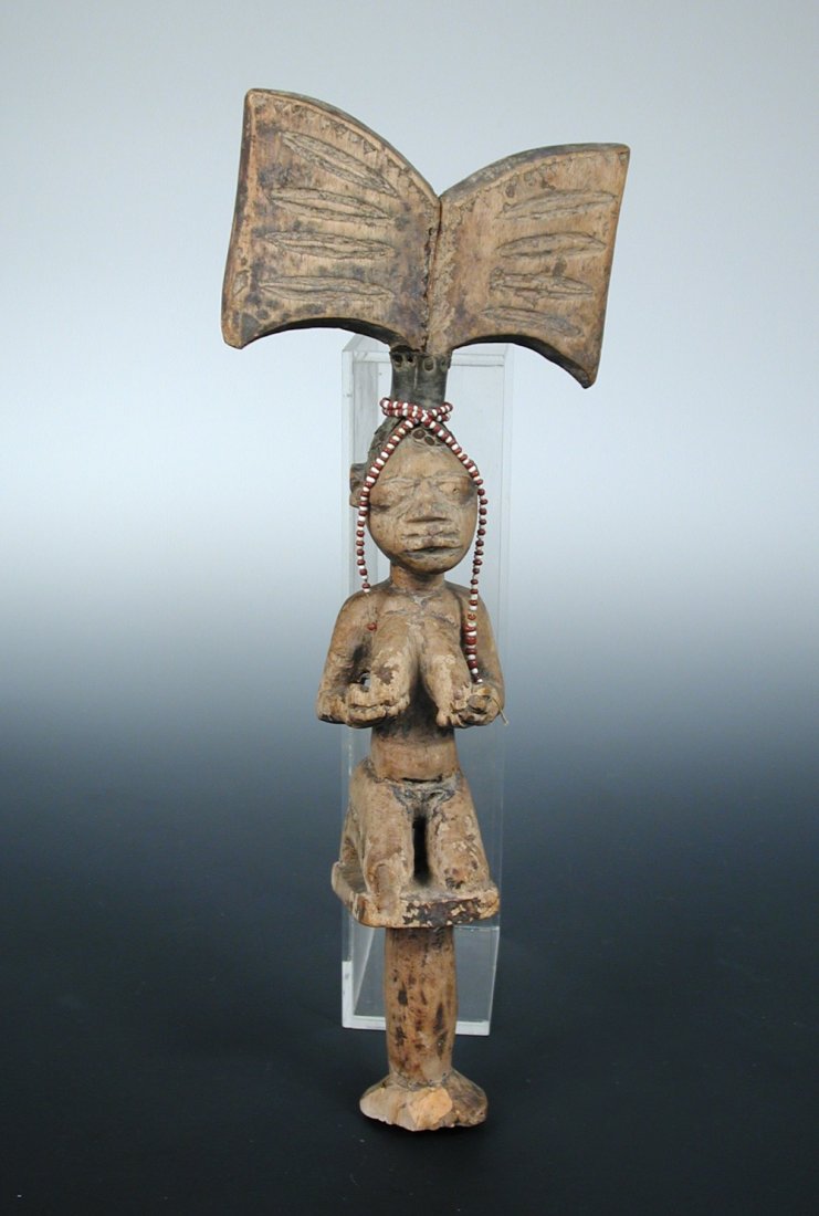 A Yoruba Shango wand, 1047,: A Yoruba Shango wand, 1047, carved as a kneeling lady wearing a bead necklace her hair raised in a butterfly shape above her head, 36cm (14.25 in) high