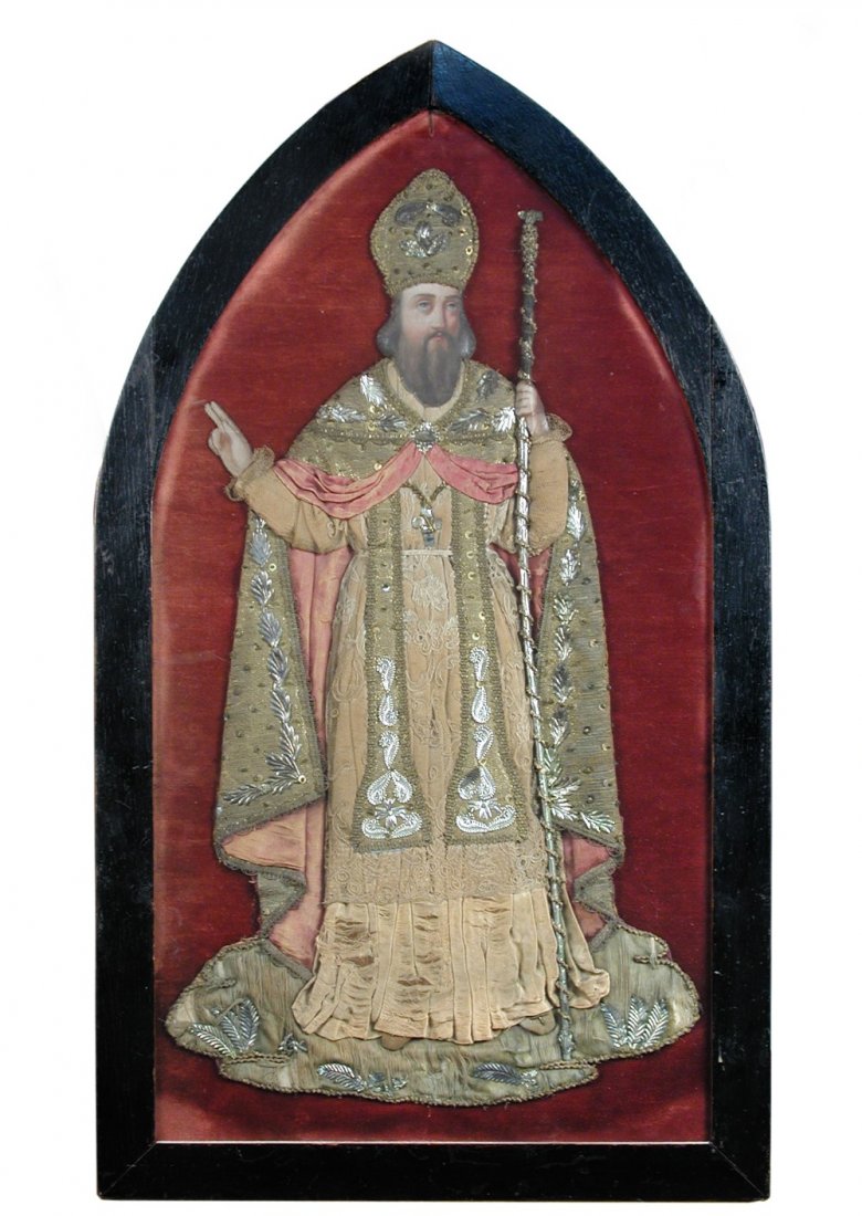 A 19th century embroidery of a Bishop: A 19th century embroidery of a Bishop standing holding a staff, his right hand raised in benediction, his silk, silver thread and muslin robes padded to rise in low relief from the crimson silk back g